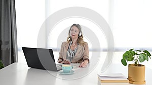 Young business woman working in the office on laptop listening the music on the headphones. Female businessperson enjoying her wor
