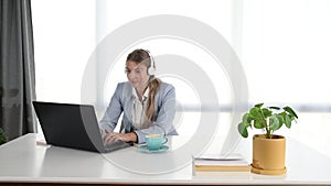 Young business woman working in the office on laptop listening the music on the headphones. Female businessperson enjoying her wor