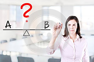 Young business woman writing A and B compare on balance bar. Office background. photo