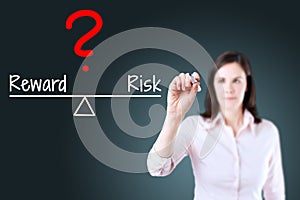 Young business woman writing question with risk compare to reward on balance bar. Blue background. photo