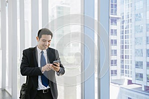 Young businessman in airport. Casual urban professional business man using smartphone smiling happy inside office building.