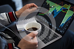 Young businessman analysing finance on laptop with coffe in hand.