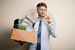 Young businessman with beard fired holding cardboard standing over white background serious face thinking about question, very