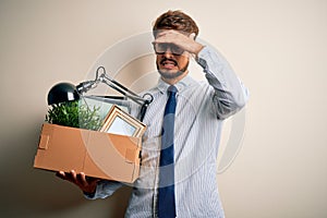 Young businessman with beard fired holding cardboard standing over white background stressed with hand on head, shocked with shame