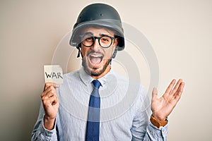 Young businessman with beard wearing helmet holding paper with war message very happy and excited, winner expression celebrating