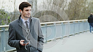 Young businessman being outdoors and using headphones while a pleasant phone call