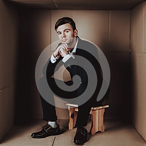 Young Businessman in Black Suit in Cardboard Box.