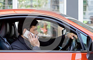 Young businessman in a black suit using mobile phone while holding the car wheel