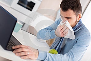 young businessman blows nose while working on laptop