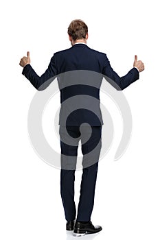 Young businessman in blue navy suit making thumbs up sign