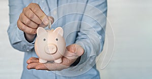 a young businessman in a blue shirt puts a coin in the piggy bank. The concept of saving money. copy space