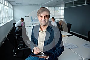 Young businessman in businesswear sitting on desk with digital tablet and digitized pen in office