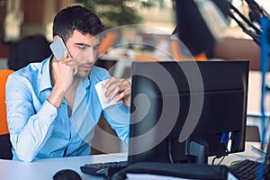 Young businessman busy working on laptop computer while talking on the smart-phone at office.