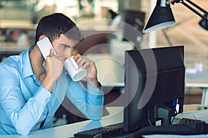 Young businessman busy working on laptop computer while talking on the smart-phone at office.