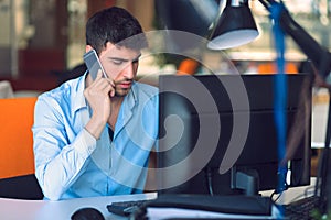Young businessman busy working on laptop computer while talking on the smart-phone at office.