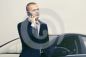 Young businessman calling on cell phone next to his car