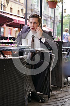 A young businessman came to lunch in a cafe, he sits at a table and talking by smartphone with bad emotions