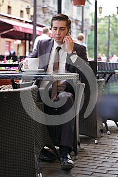 A young businessman came to lunch in a cafe, he sits at a table and talking by smartphone with bad emotions