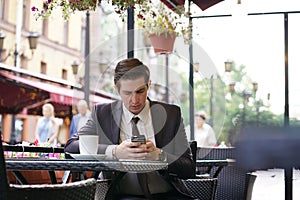 A young businessman came to lunch in a cafe, he sits at a table and talking by smartphone with bad emotions