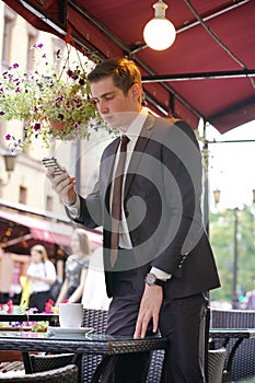 A young businessman came to lunch in a cafe, he sits at a table and talking by smartphone with bad emotions