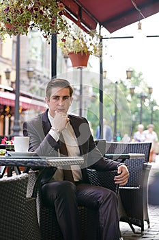A young businessman came to lunch in a cafe, he sits at a table and talking by smartphone with bad emotions