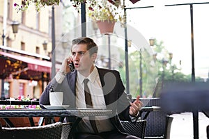 A young businessman came to lunch in a cafe, he sits at a table and talking by smartphone with bad emotions