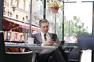 A young businessman came to lunch in a cafe, he sits at a table and talking by smartphone with bad emotions