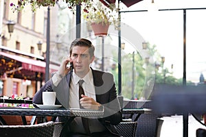 A young businessman came to lunch in a cafe, he sits at a table and talking by smartphone with bad emotions