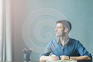 Young businessman caucasians sitting at desk office table and taking notes in notebook. Writing and looking out the window