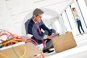 Young businessman crouching while using laptop on cardboard box in new office