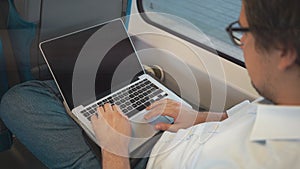 Young businessman with dark hair using his laptop while riding a train to work.