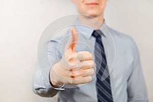 Young businessman dressed in blue shirt and tie shows thumb up close up, on gray background