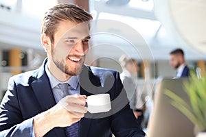 Young businessman drinking coffee in office while typing on computer.