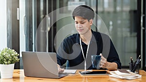 Young businessman drinking coffee and working using laptop and documents