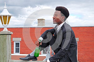 Young businessman drinking wine bottle on roof success suit and tie