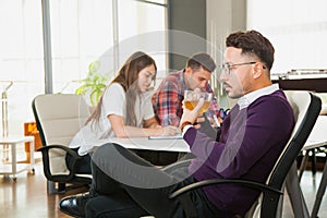 Young businessman drinks tea while his collegues on backgroung work hard