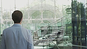 A young businessman, an employee of a large company walks around a modern beautiful office and greets, waves his hand