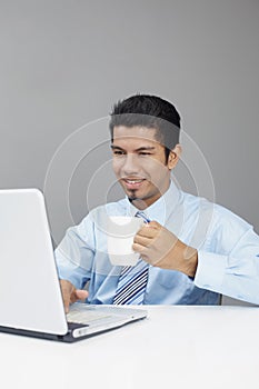 Young businessman enjoying a cup of coffee while working on laptop. Conceptual image