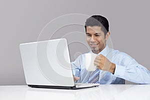 Young businessman enjoying a cup of coffee while working on laptop. Conceptual image