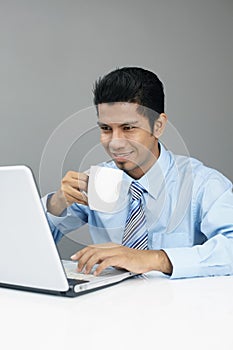 Young businessman enjoying a cup of coffee while working on laptop. Conceptual image