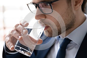 Young businessman in eyeglasses drinking glass of fresh water.