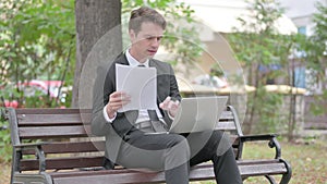 Young Businessman Feeling Upset while Reading Contract and Using Laptop Outdoor
