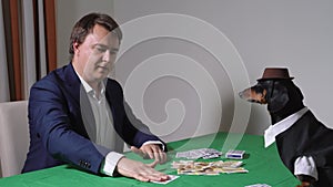 Young businessman in formal suit hands out cards for gambling or shows tricks to funny dachshund dog in jacket and wide