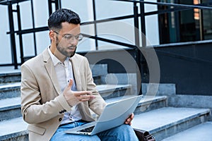 Young businessman in formal wear sitting on the stairs out of office building working on laptop computer. Job candidate work on