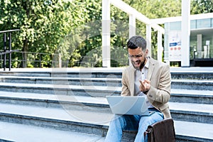 Young businessman in formal wear sitting on the stairs out of office building working on laptop computer. Job candidate work on