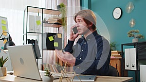 Young businessman freelancer answering to client on mobile phone call, using smartphone and laptop