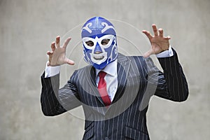 Young businessman gesturing in wrestling mask and pinstripes suit over gray background
