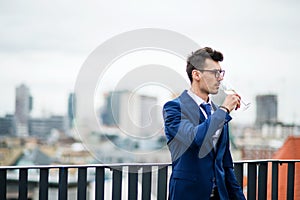 A young businessman with glass on a party outdoors on roof terrace in city.