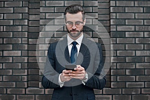 A young businessman in glasses and an expensive suit, works on a smarphone in his hands