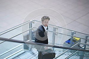 Young businessman going down a stairway with his suitcase, lookin up